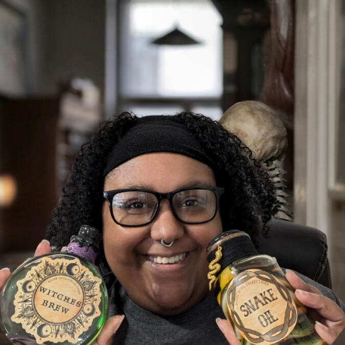 Owner holding witches brew potion bottle and snake oil apothecary bottle.